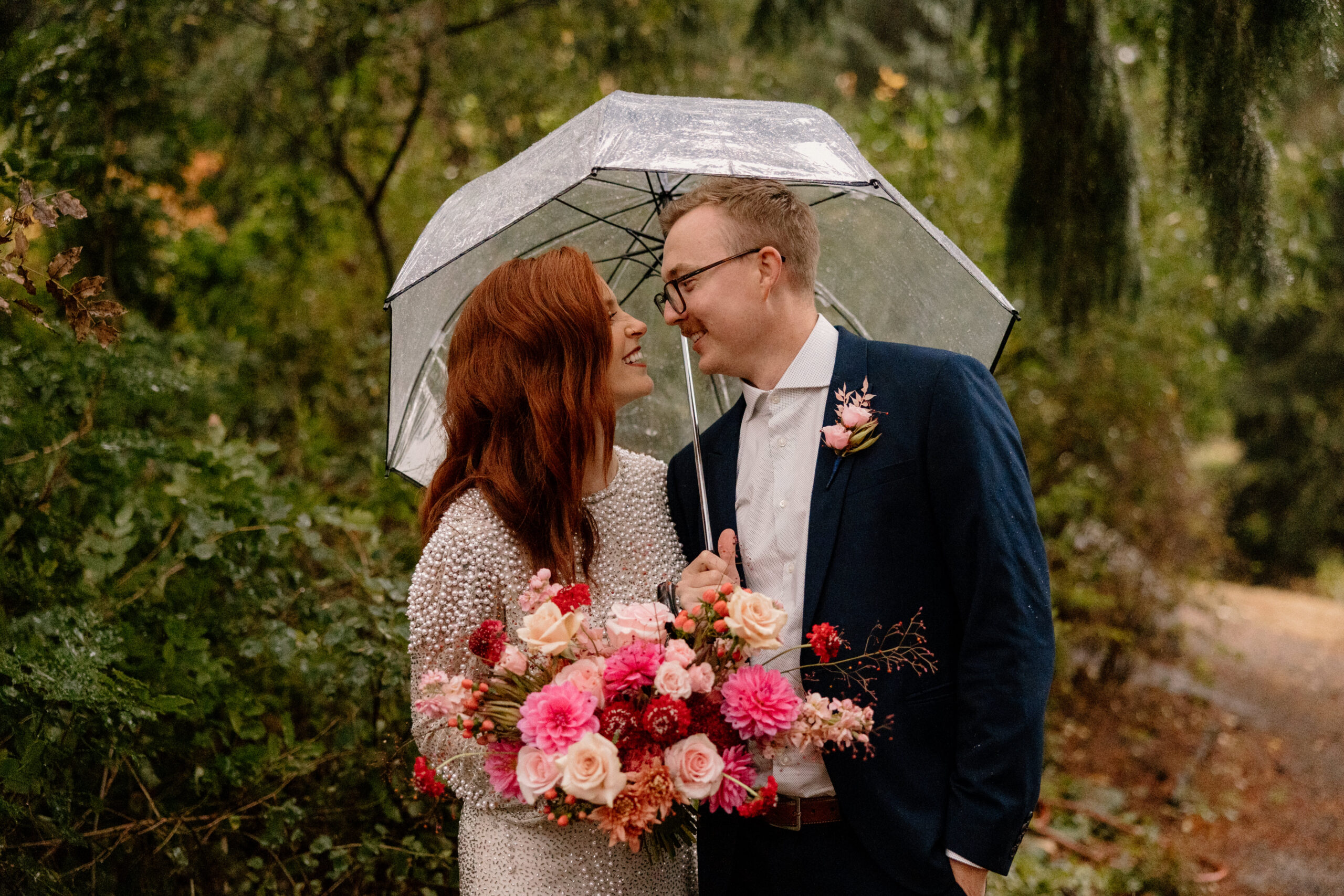 A laughing couple taking photos in the rain during their Hoyt Arboretum elopement.