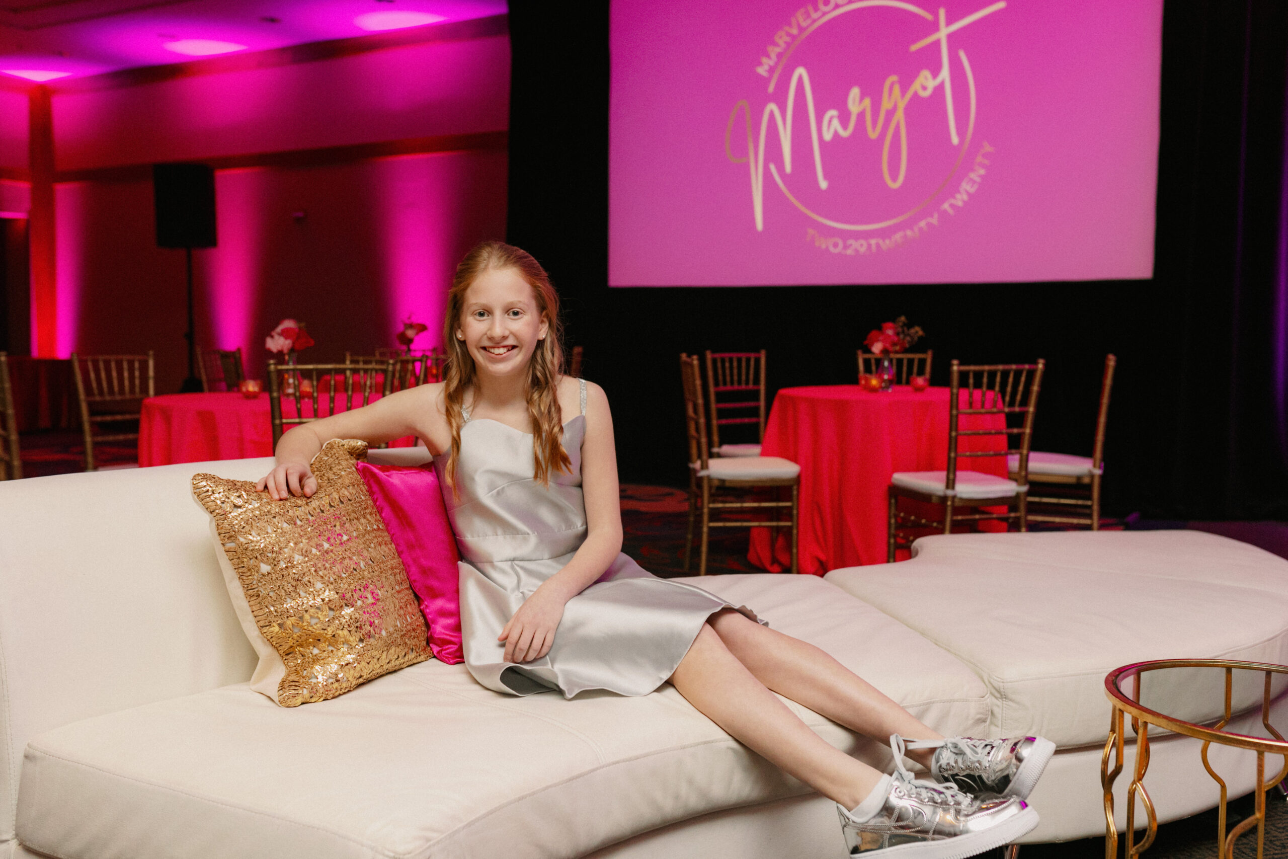 A girl poses in front of her pink themed bat mitzvah party decor.